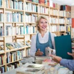 femme souriante debout entourée de livres et d'étagères